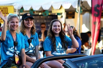 Three students posed in a convertable during a parade