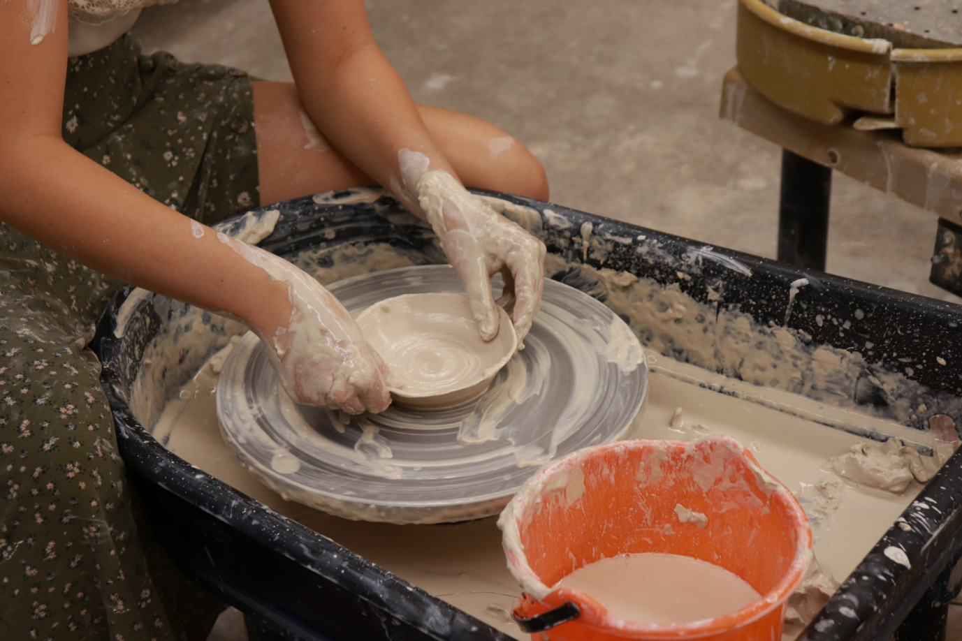 A student making a clay bowl on a pottery wheel