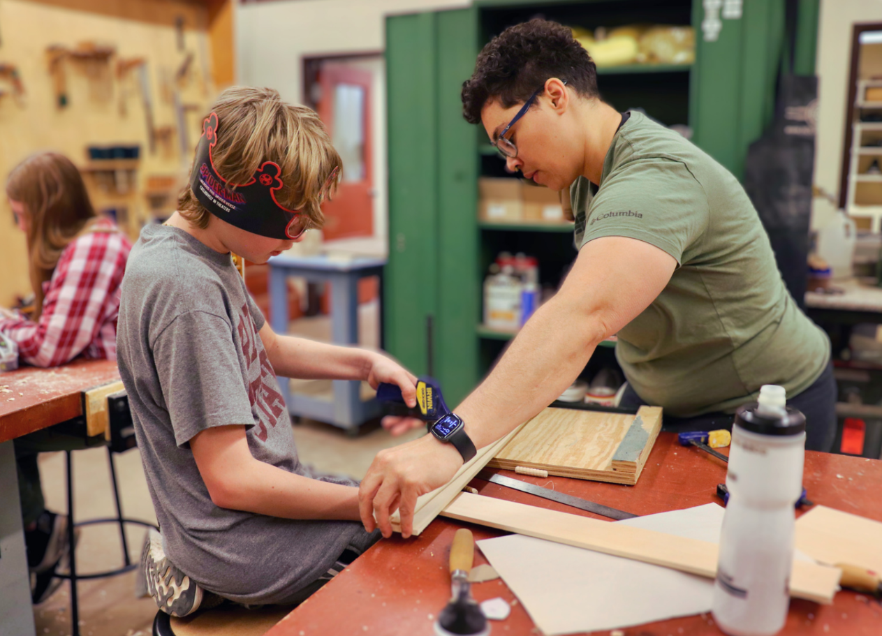 A student works on a woodworking project with the help of an instructor
